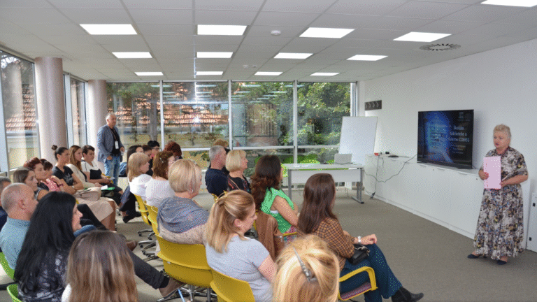 A person speaking to a group of people in a room Description automatically generated with medium confidence